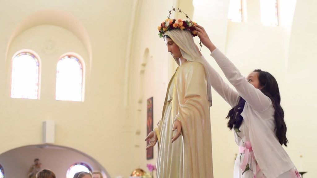 Una niña corona de flores a la Virgen María.