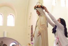 Una niña corona de flores a la Virgen María.
