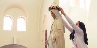Una niña corona de flores a la Virgen María.